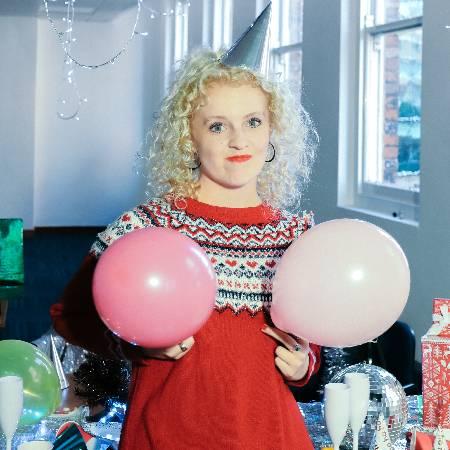 Brogan wearing a Christmas jumper and holding two balloons in front of her chest