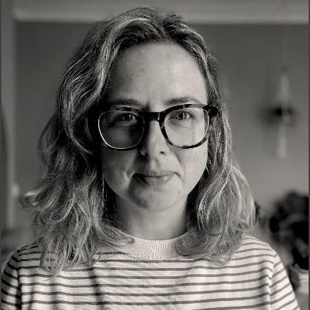 Portrait headshot photograph of Verity Quinn - wearing glasses and a striped top , shoulder length hair and looking to camera.