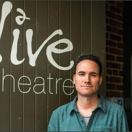 Portrait headshot of Jack McNamara standing in front of Live Theatre's door - dressed in a green open necked shirt and looking to camera.