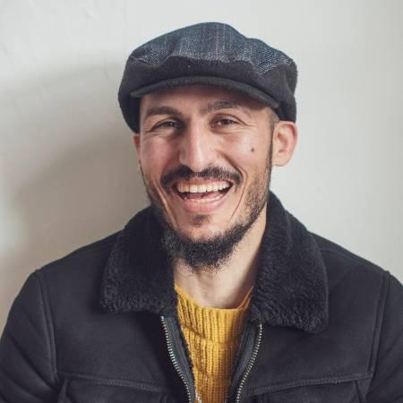 Portrait photograph of Hamzeh Al Hussien - looking to camera dressed in a yellow jumper, jacket and wearing a cap