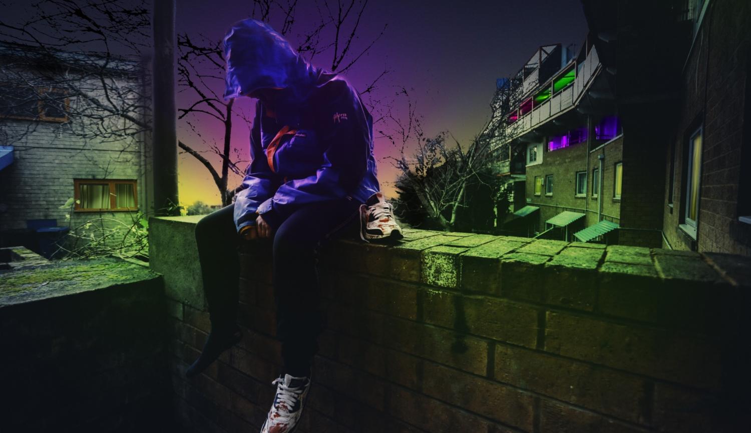 A young man sits on a wall at night wearing a hoodie, with a bloodied trainer next to him