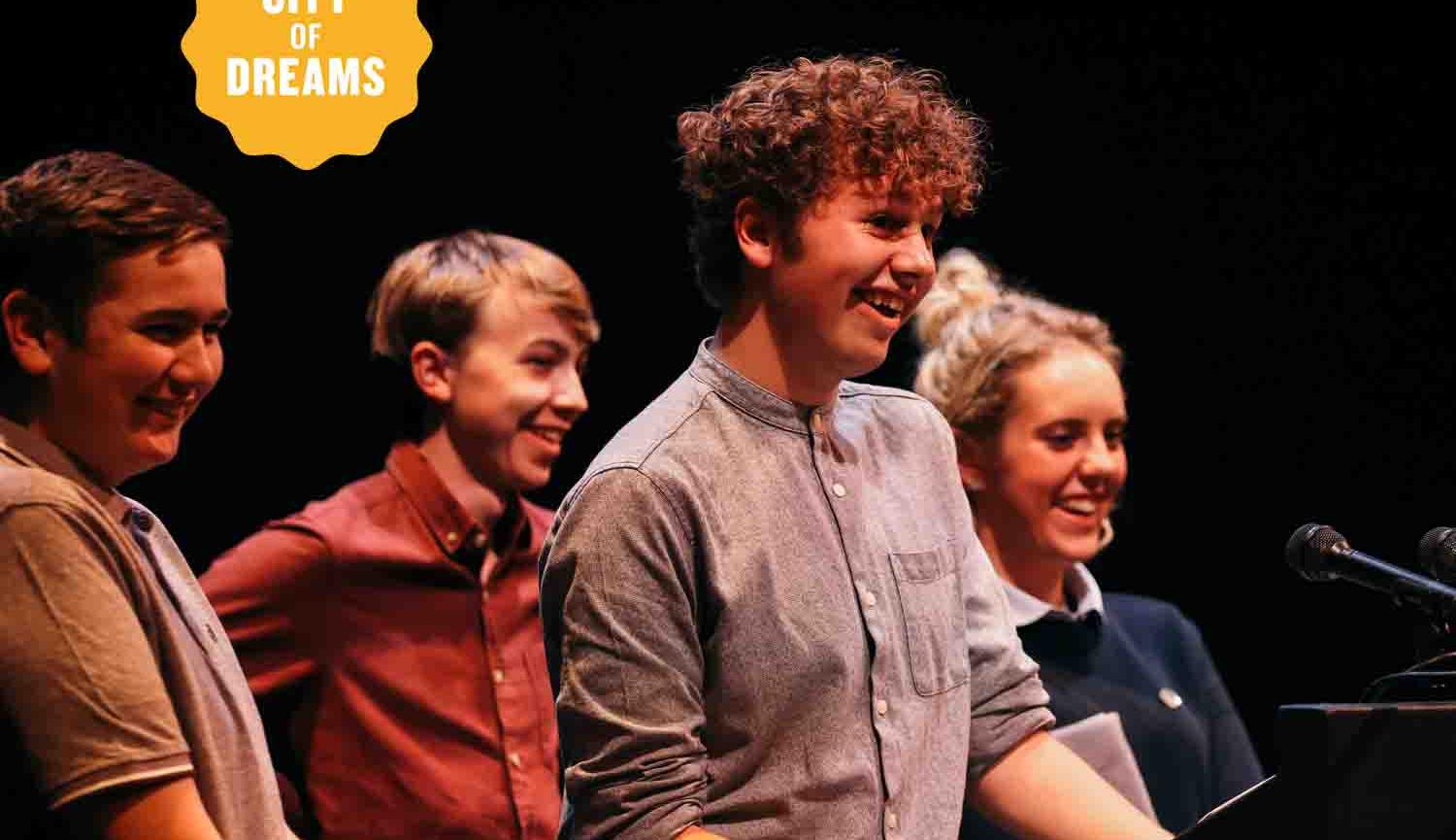 Photo of four young people standing on stage facing to right