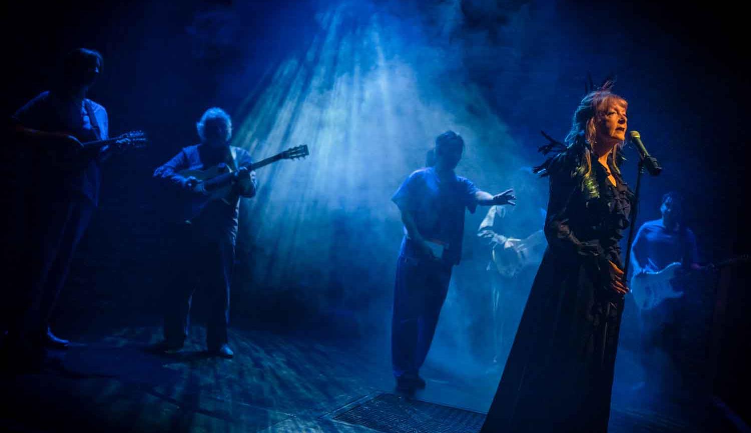 Photo of woman on stage singing into microphone with musicians in background