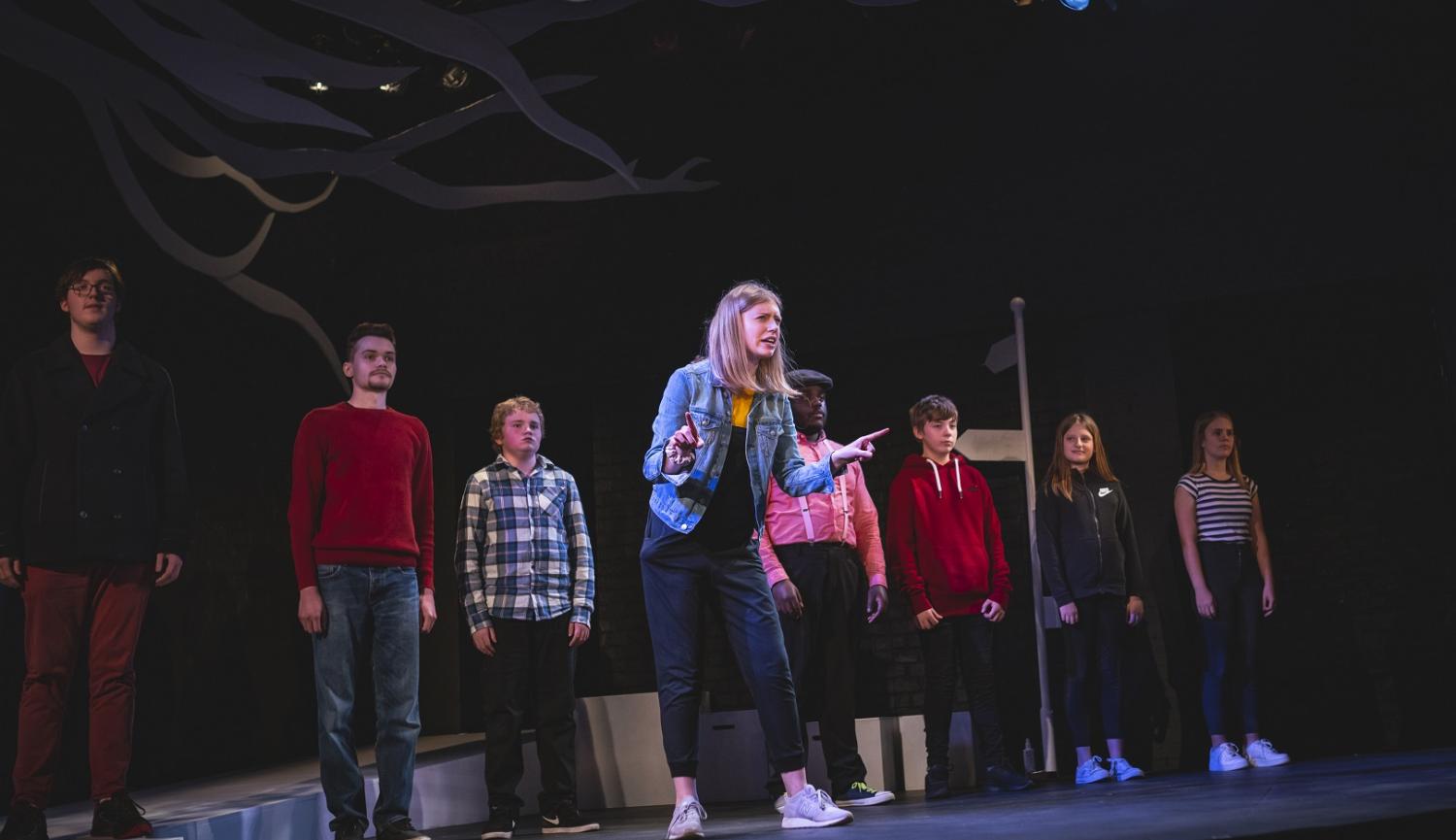 Line of young people on stage with one forward of the rest talking