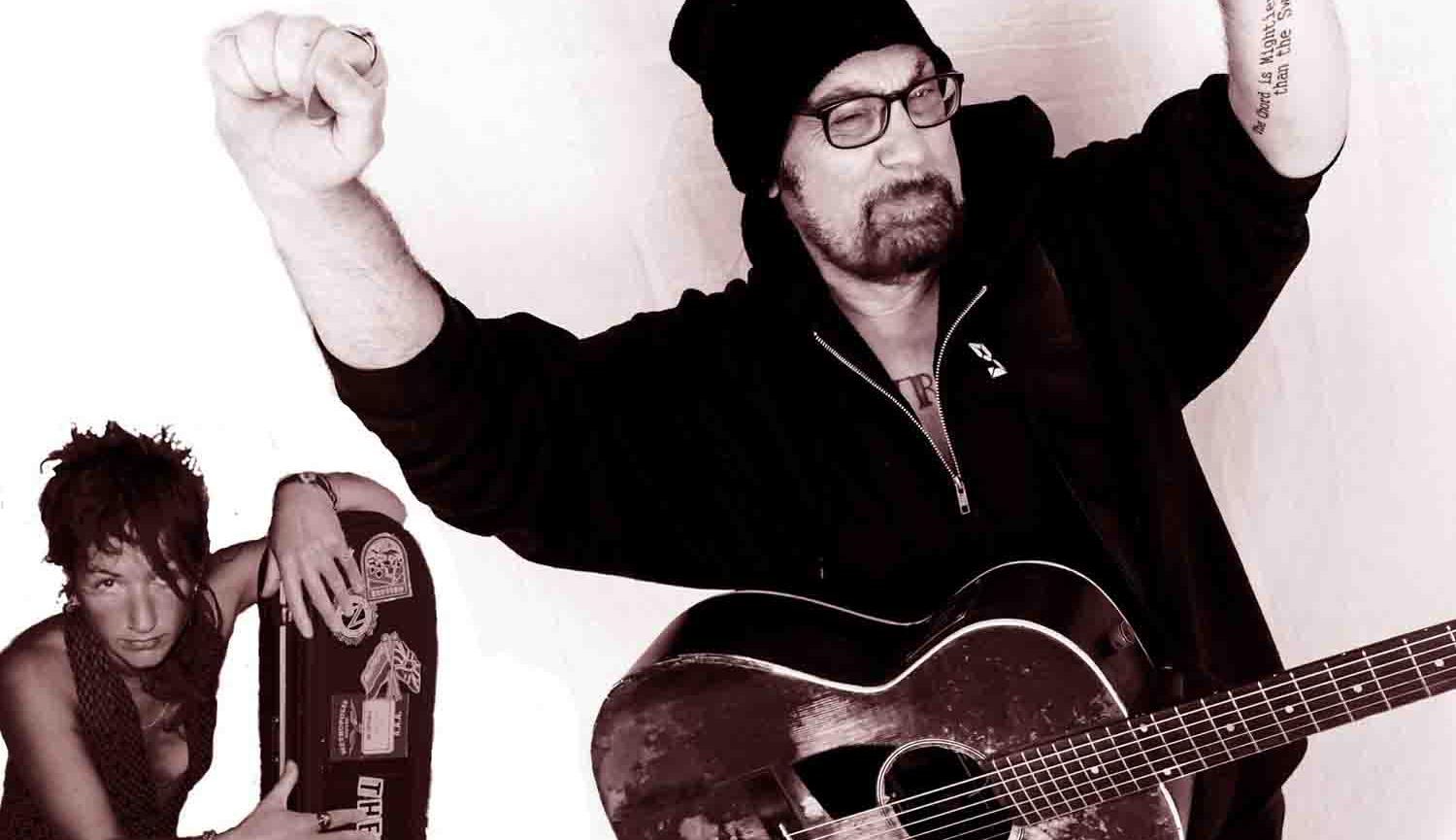 Black and white photo of man with guitar, hands in air, with woman crouching in background