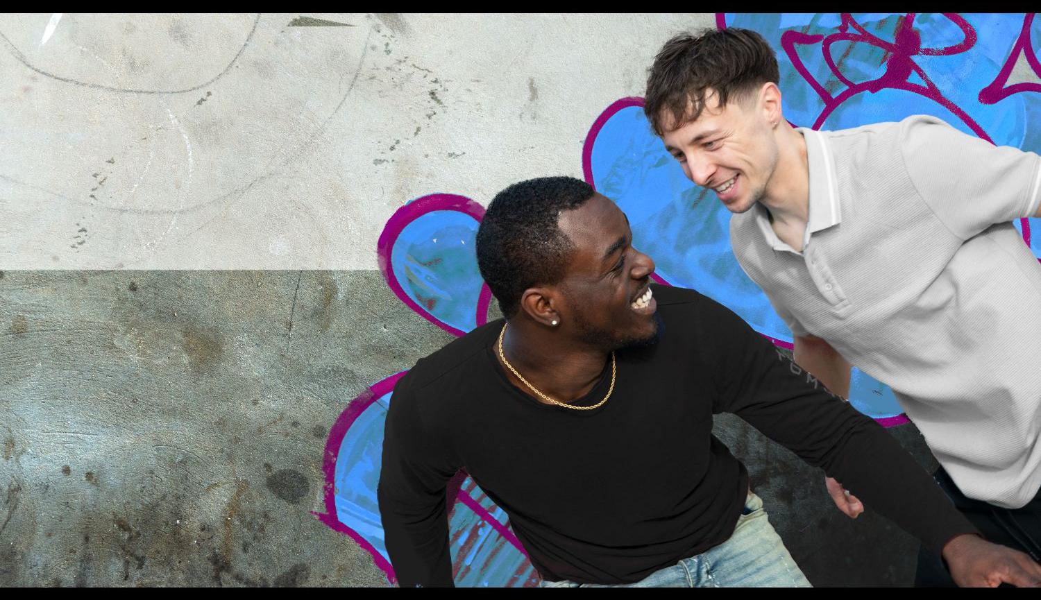 Two men standing in front of a wall with grafitti on