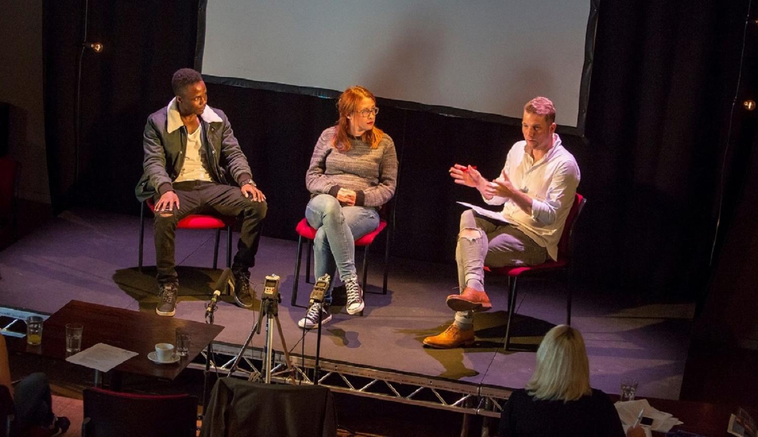 3 people sitting on chairs on stage