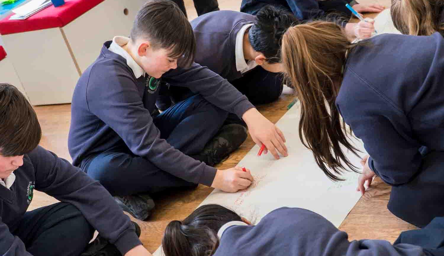 Photo of children sitting on floor around a piece of paper writing on it