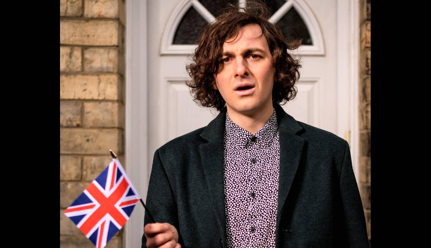 Rowan McCabe Poet standing in front of a door holding a Union Jack 