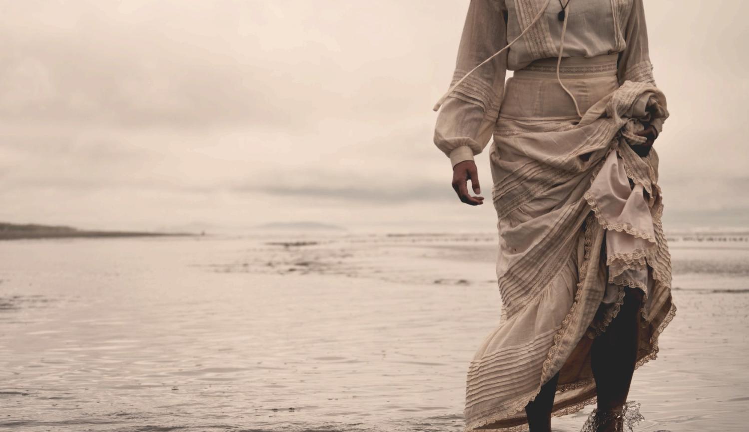 A women in a long white dress standing in the water's edge