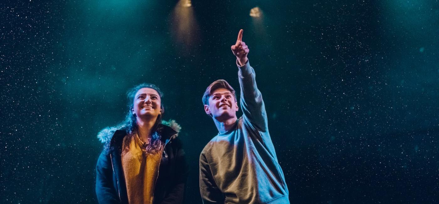 A young lady and young man on stage - the man is pointing to something high up in the distance