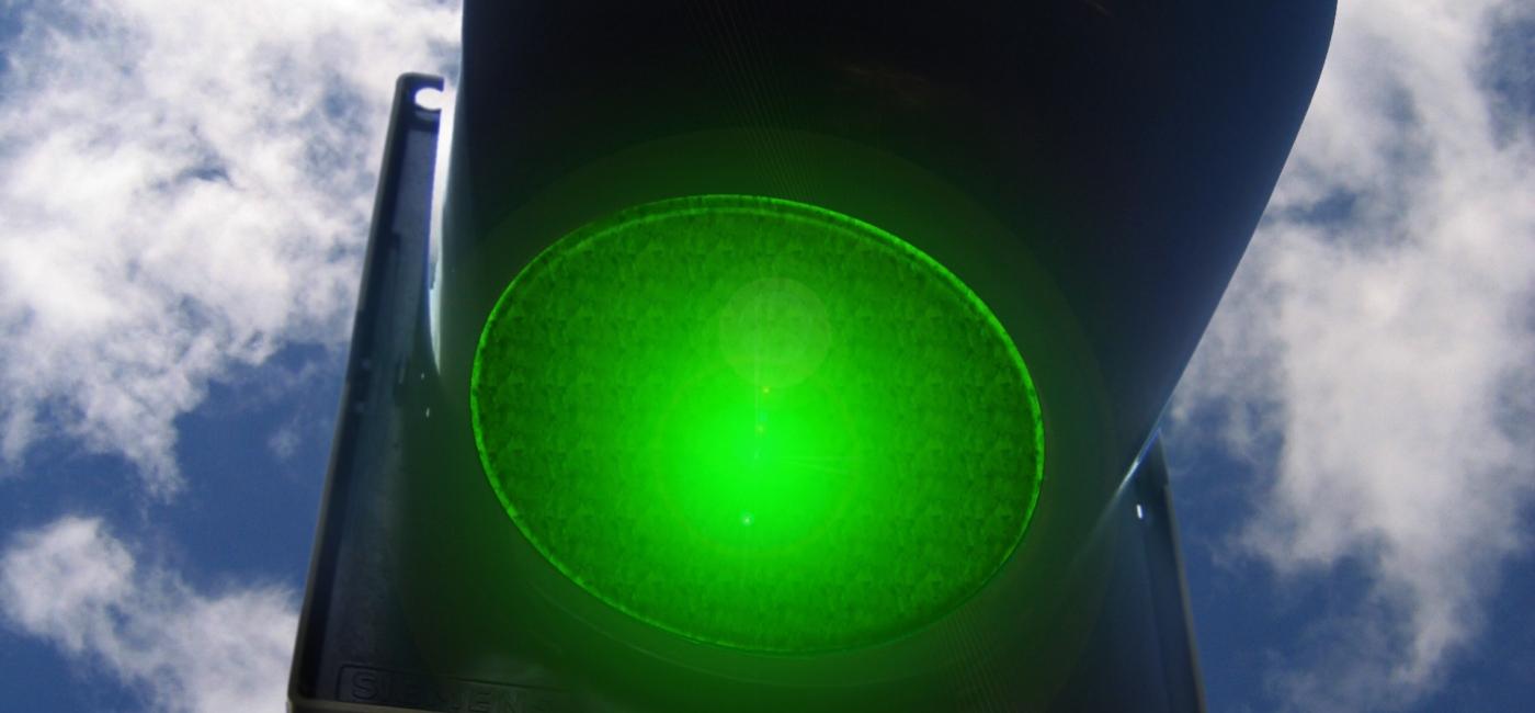 Green traffic light with blue sky and clouds in background