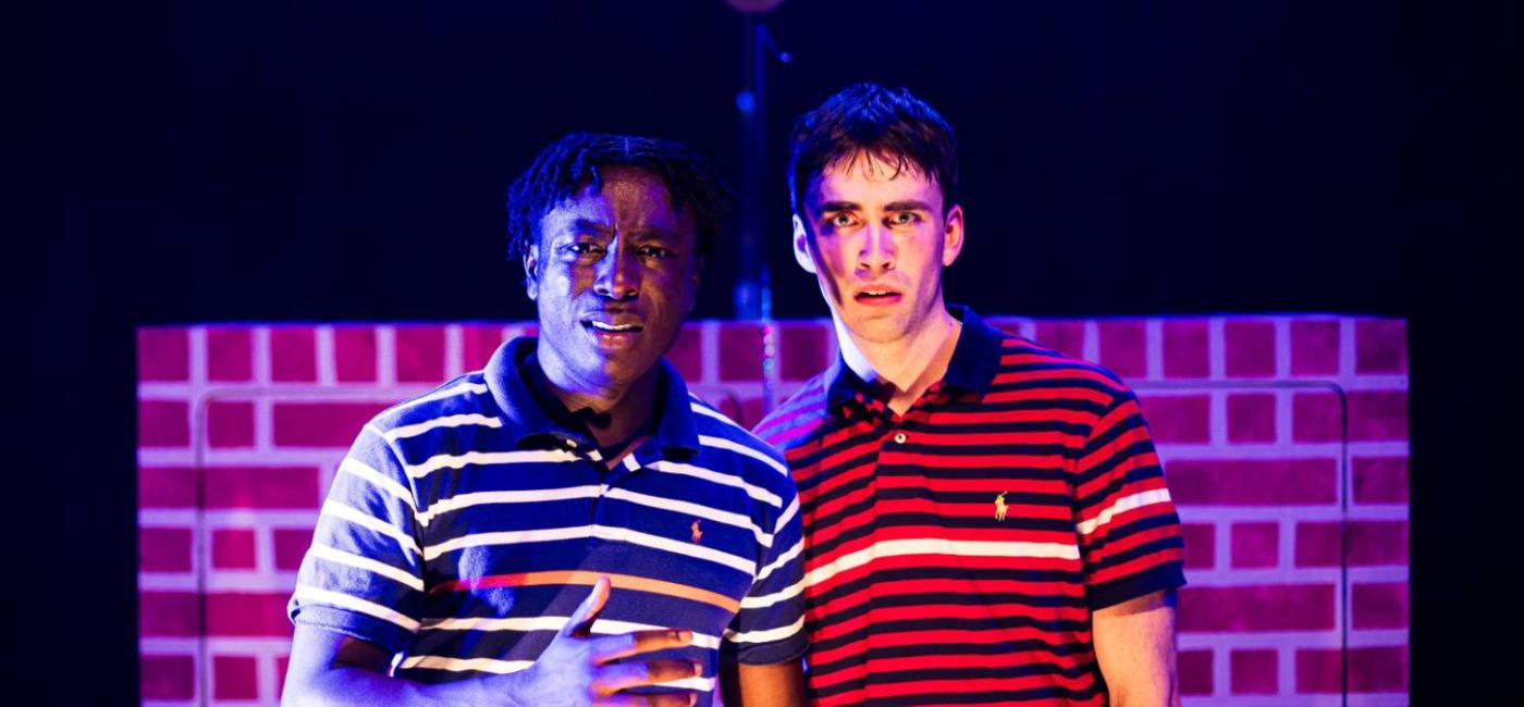 Two males looking to camera in front of a brick wall
