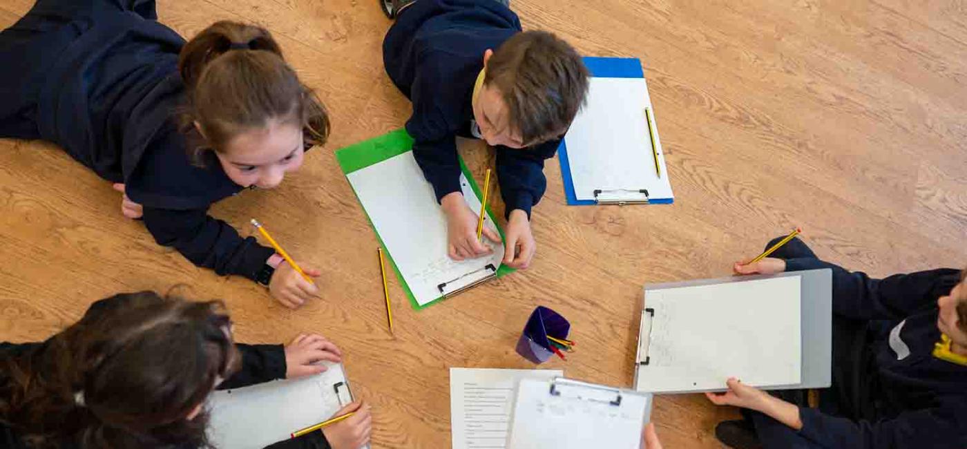 Group of school children lying on floor writing on paper on clipboards