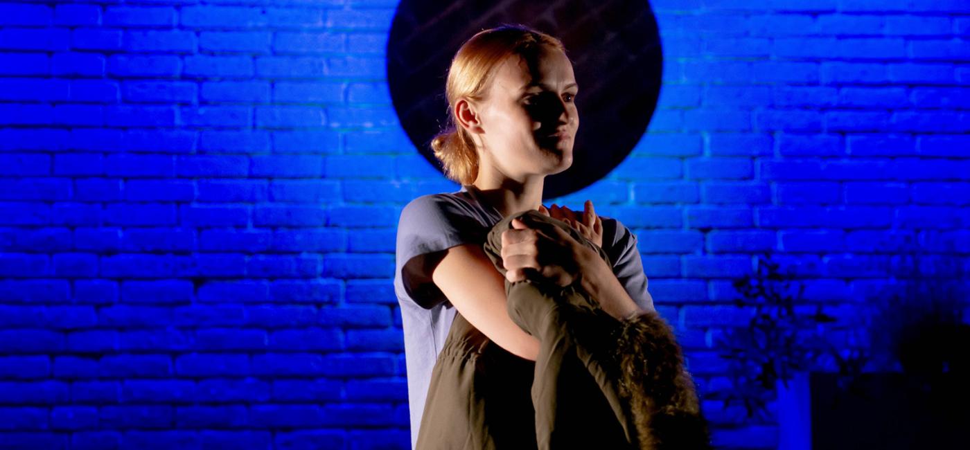 Photograph of a person standing arms crossed in front of a wall with a blue light