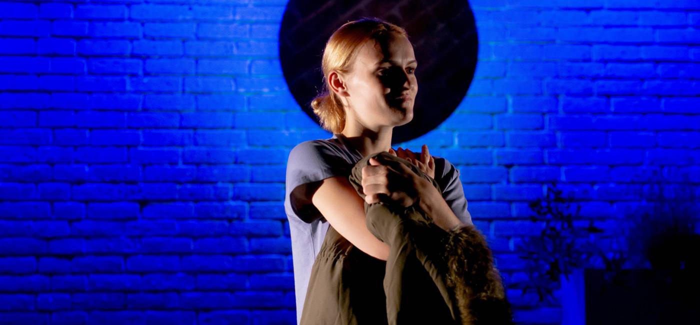 Photograph of a person standing arms crossed in front of a wall with a blue light 