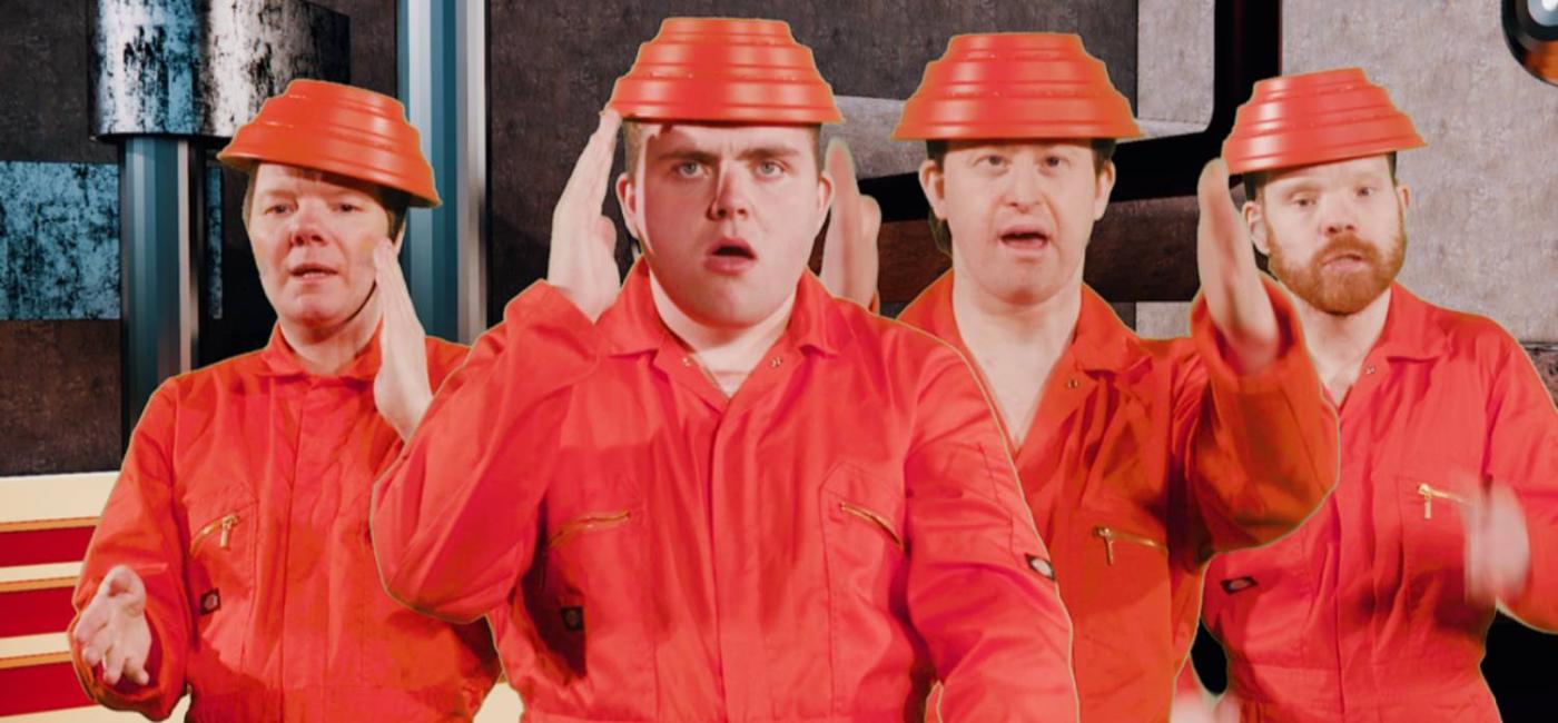 4 members of the Lawnmowers Theatre Ensemble wearing orange boiler suits and plastic hats