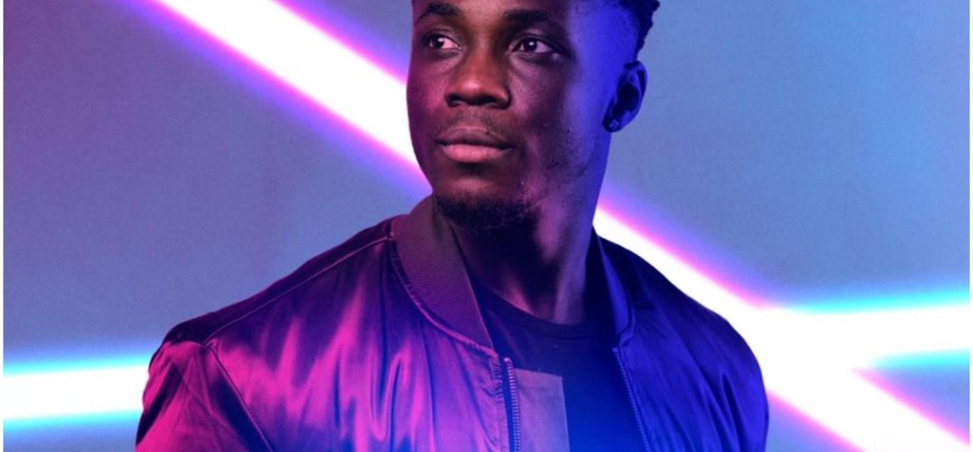 Young man on stage with 2 bright white lights behind him