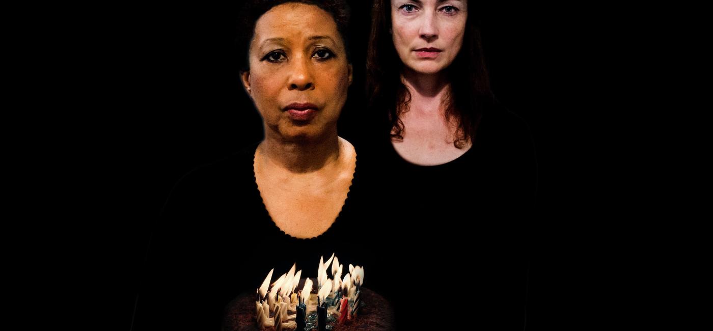 Two women in black one holding a birthday cake with lit candles