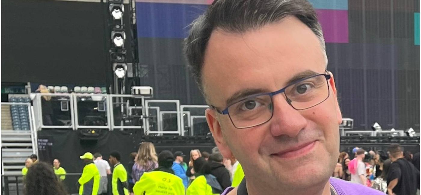 Photograph of JD Stewart looking to camera with a stage in the background