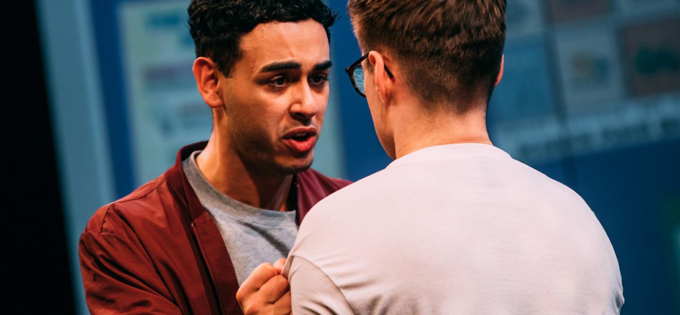 Two males, standing face to face, one gripping the other's shirt