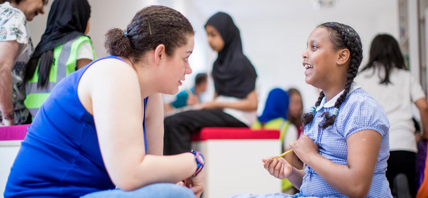 Young women and school child sitting on floor talking animatedly