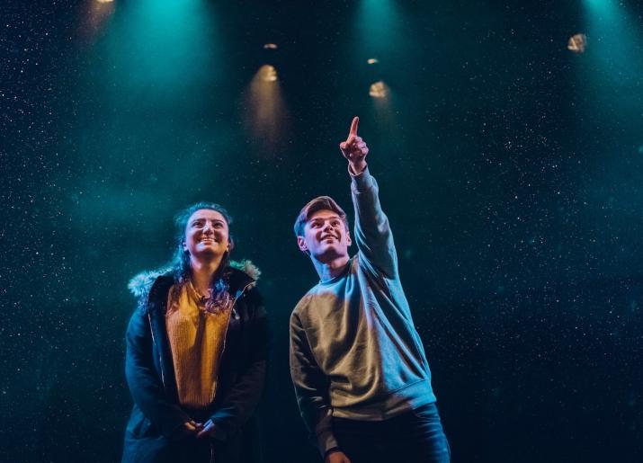 A young lady and young man on stage - the man is pointing to something high up in the distance