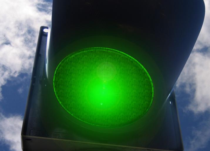 Green traffic light with blue sky and clouds in background