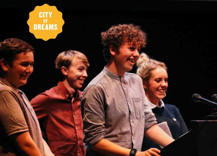 Photo of four young people standing on stage facing to right