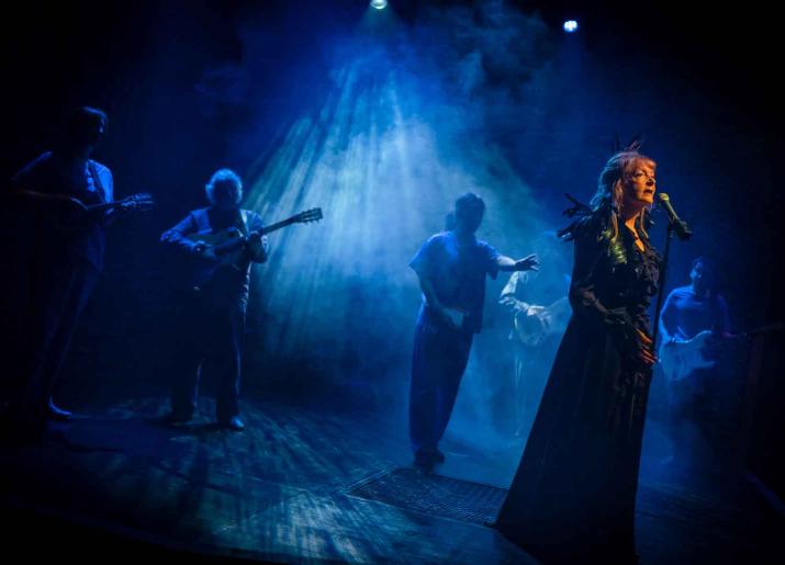 Photo of woman on stage singing into microphone with musicians in background