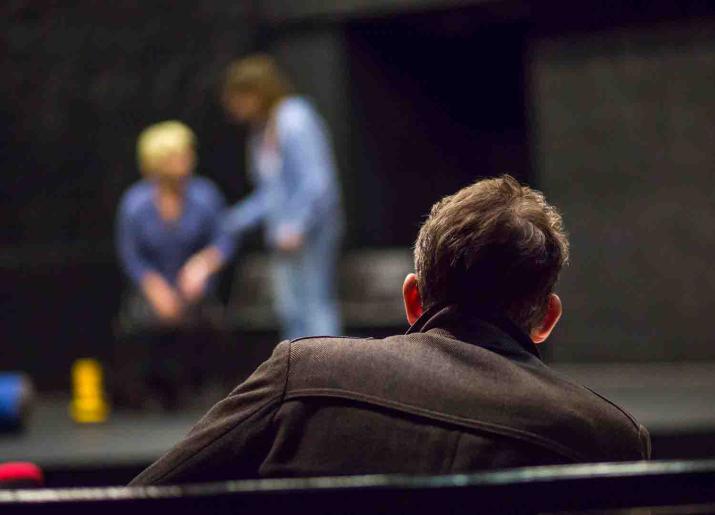 Photo of back of mans head and shoulders sitting watching two people on stage