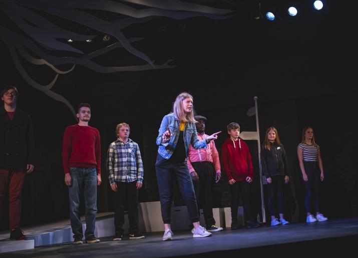 Line of young people on stage with one forward of the rest talking