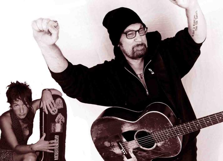 Black and white photo of man with guitar, hands in air, with woman crouching in background