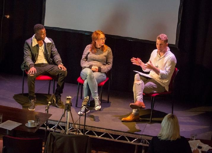 3 people sitting on chairs on stage