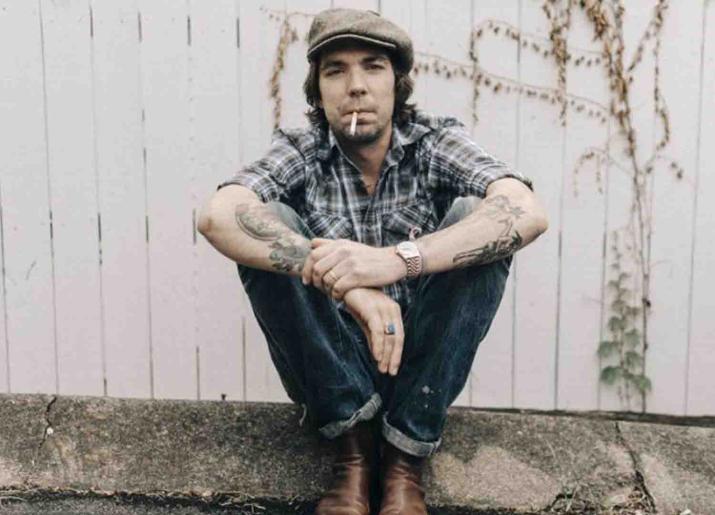 Photo of man sitting on ground against a fence