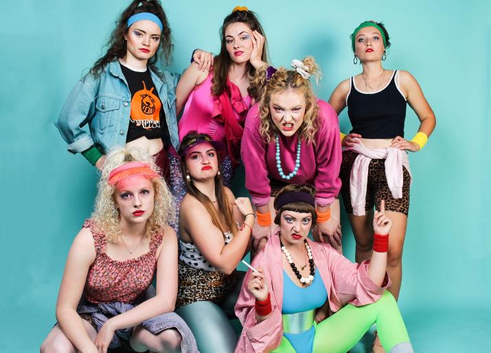 7 women dressed in 80s workout gear grimace at the camera