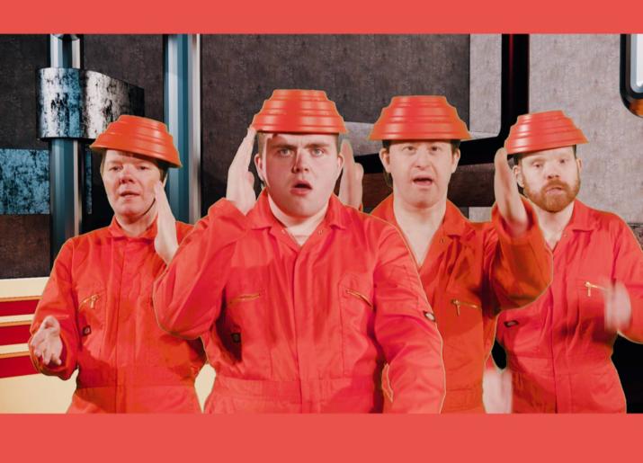 4 members of the Lawnmowers Theatre Ensemble wearing orange boiler suits and plastic hats