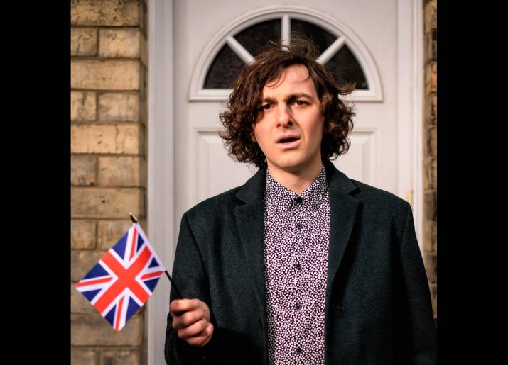 Rowan McCabe Poet standing in front of a door holding a Union Jack 