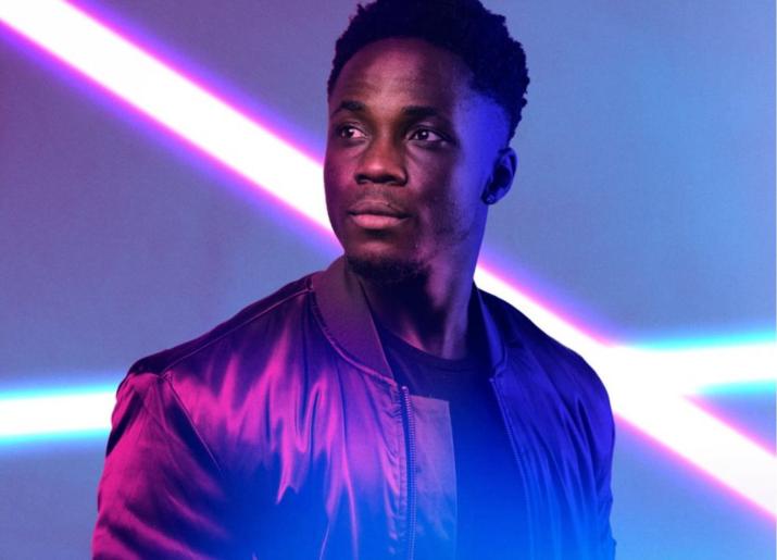 Young man on stage with 2 bright white lights behind him