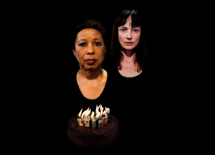 Two women in black one holding a birthday cake with lit candles