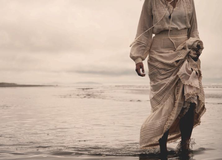 A women in a long white dress standing in the water's edge