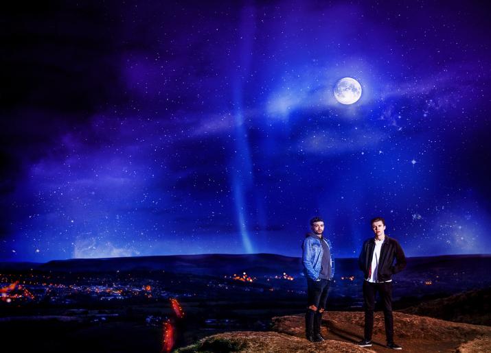 Two men on hilliside at night with moon overhead