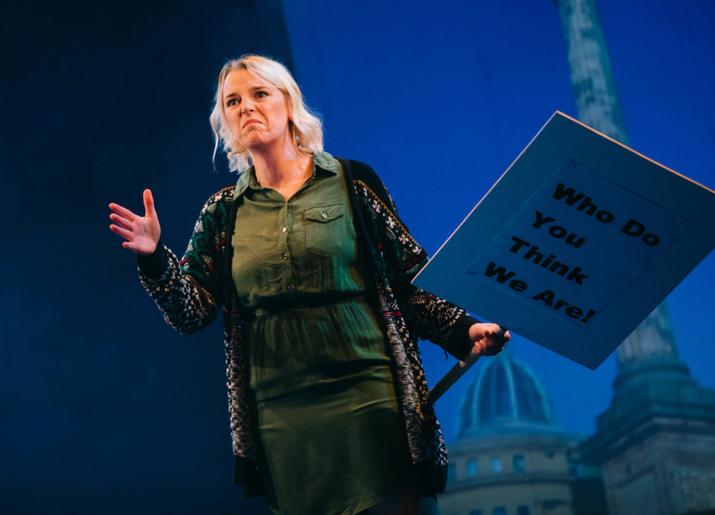 Woman holding a placard in front of Grey's Monument looking to camera 