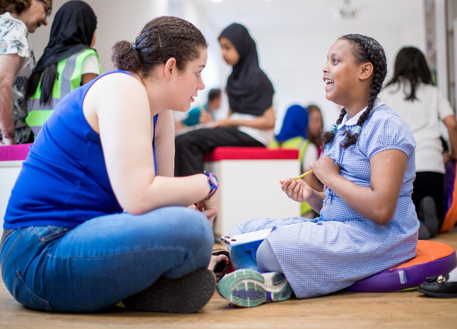 Young women and school child sitting on floor talking animatedly